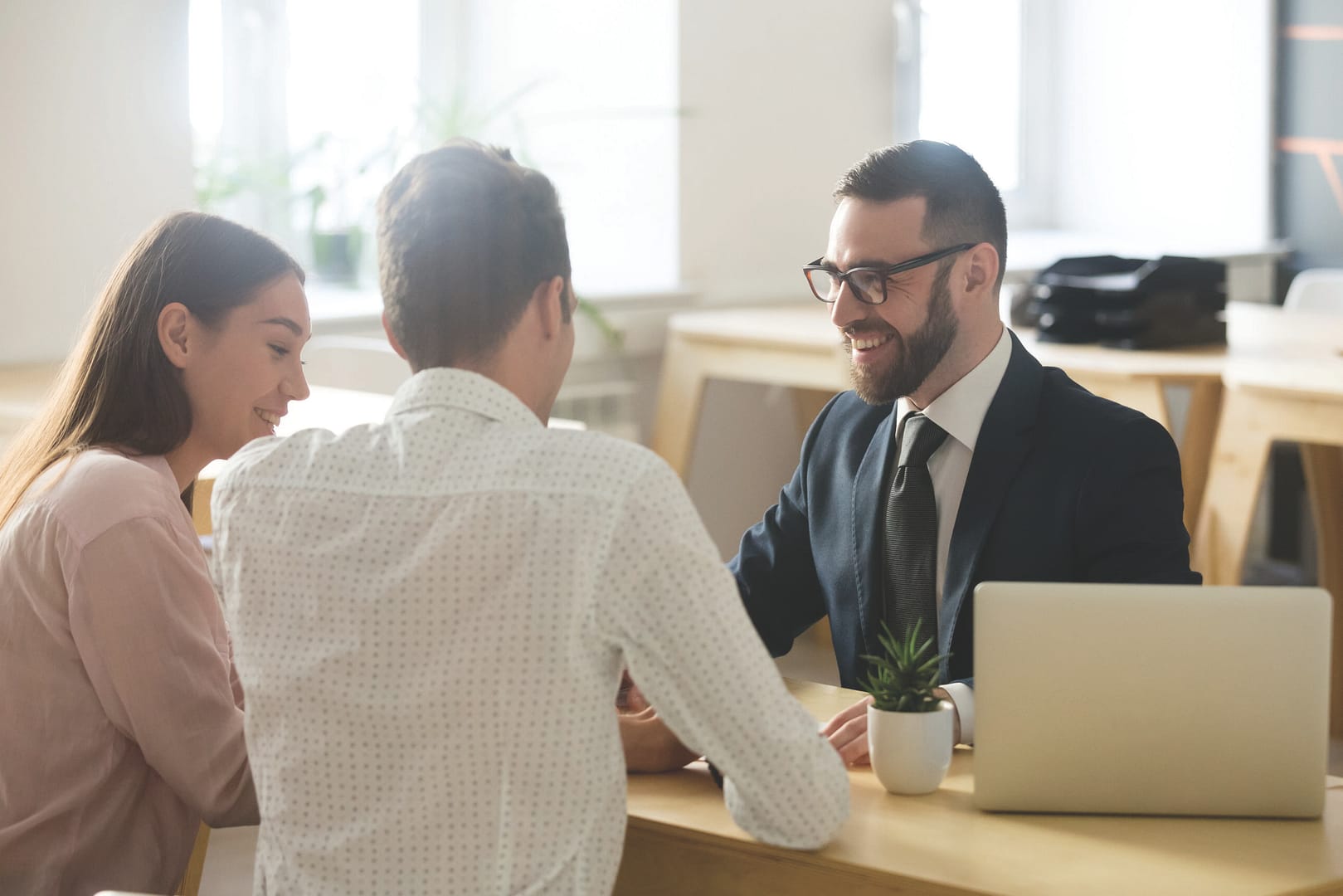 Friendly lawyer or financial advisor in suit consulting young couple, smiling investment broker or bank worker making loan offer, giving legal advice, selling insurance or real estate to customers